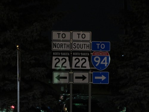 Road signs at night indicating directions to North Dakota, with routes 22 and 94.