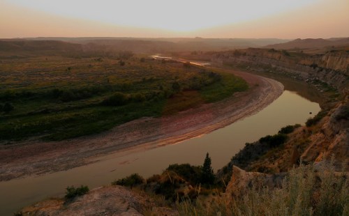 A serene river winding through a lush valley at sunset, with soft light illuminating the landscape.