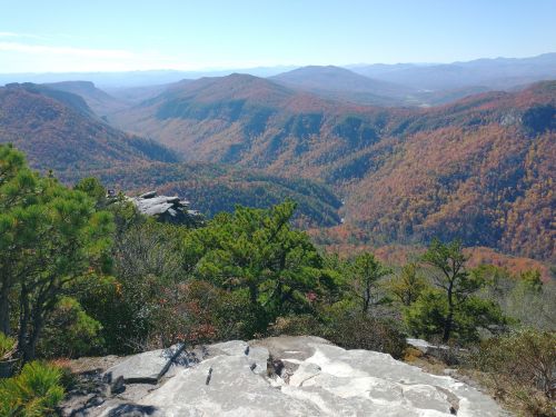 A panoramic view of colorful autumn mountains and valleys, with rocky outcrops and green trees in the foreground.