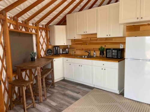 Cozy kitchen in a yurt with wooden accents, featuring a fridge, microwave, sink, and a small dining table.