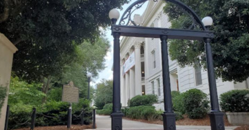 A decorative archway frames a path leading to a historic building surrounded by greenery.