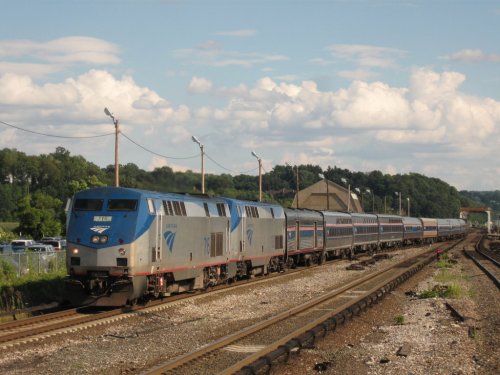 Amtrak train traveling along tracks with a blue sky and clouds in the background.