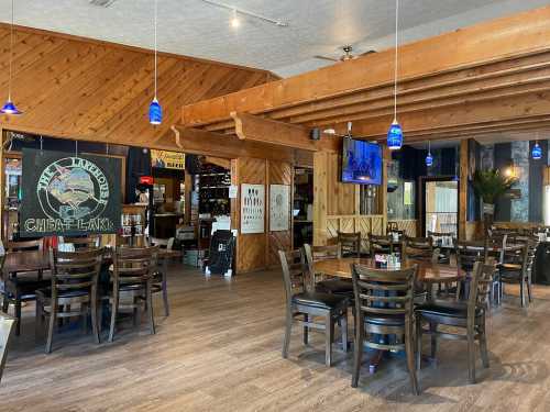 Interior of a restaurant featuring wooden decor, tables, and blue pendant lights, with a bar area in the background.