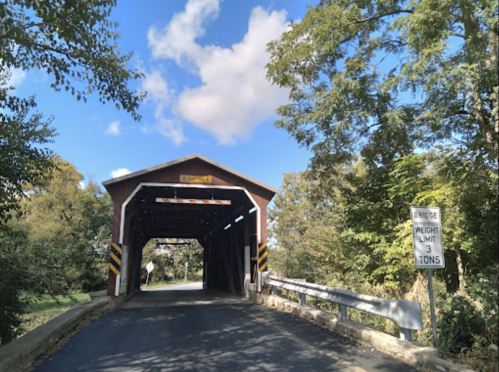 A covered bridge with a sign indicating a weight limit of 3 tons, surrounded by trees and a blue sky.