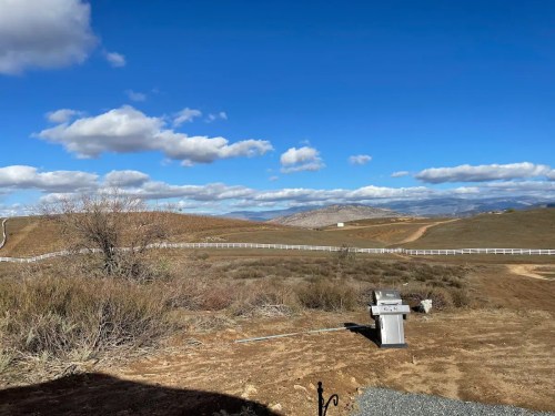 A scenic view of rolling hills under a blue sky with clouds, featuring a grill in the foreground.