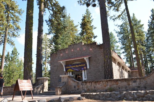 A stone building labeled "Museum" surrounded by tall trees, with a sign for the Lassen Dark Sky Festival in front.