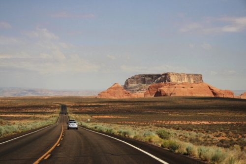 A winding road leads to a distant rock formation under a clear sky in a vast desert landscape.