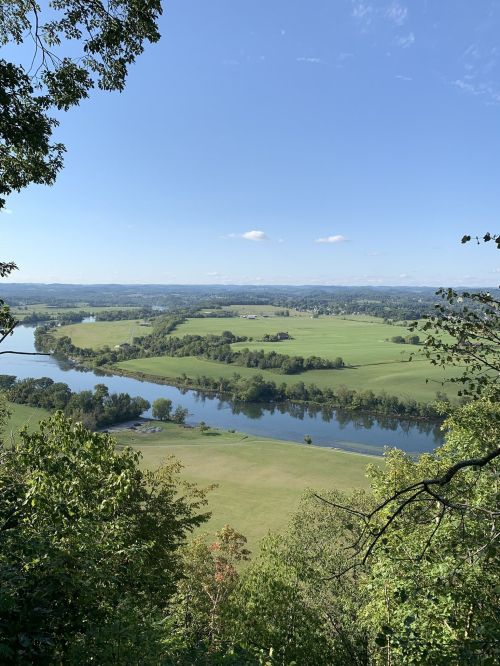 A scenic view of a river winding through lush green fields and trees under a clear blue sky.