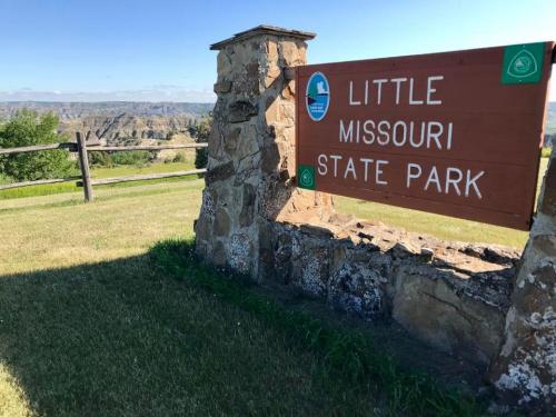 Sign for Little Missouri State Park with scenic landscape in the background and clear blue sky.