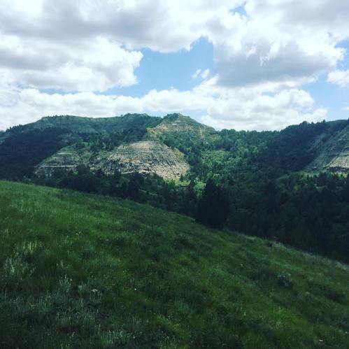 Lush green hills under a partly cloudy sky, with rocky formations in the background.