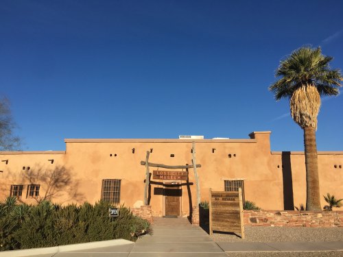 Exterior of the Lost Trail Museum, featuring adobe architecture and a palm tree under a clear blue sky.