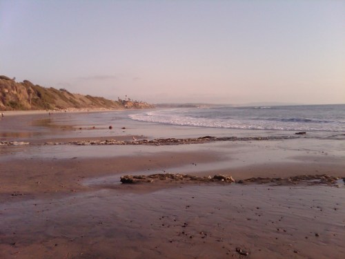 A serene beach scene with gentle waves, sandy shore, and distant cliffs under a soft, pastel sky.