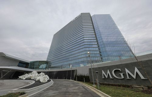 Modern glass skyscraper with "MGM" signage, featuring a sculptural installation in the foreground and cloudy sky.
