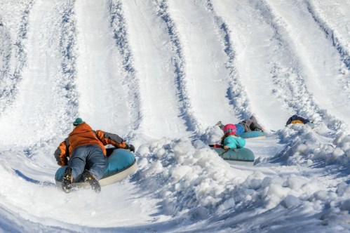 People sledding down a snowy hill on inflatable tubes, enjoying a winter day.