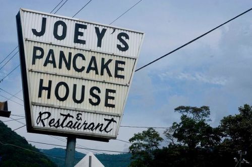 Sign for Joey's Pancake House & Restaurant against a cloudy sky, surrounded by trees.