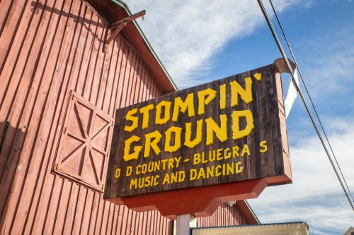 Sign for "Stompin' Ground," featuring country and bluegrass music and dancing, against a rustic wooden background.