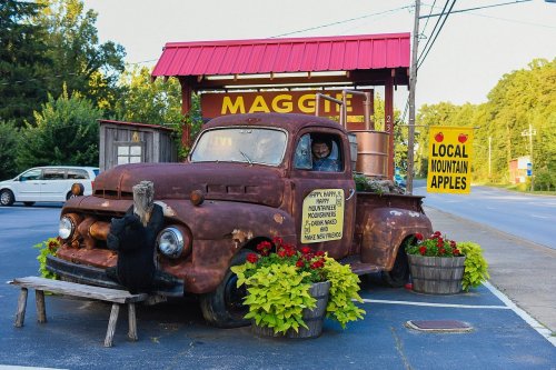 A vintage truck converted into a roadside stand selling local mountain apples, surrounded by colorful flowers.