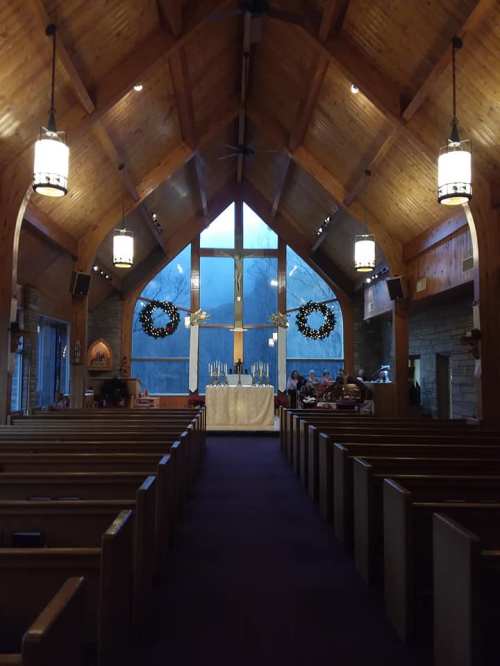 Interior of a church with wooden beams, a large cross, candles, and festive wreaths, creating a serene atmosphere.