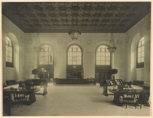 Historic interior of a grand hall featuring large windows, ornate ceiling, and wooden tables.