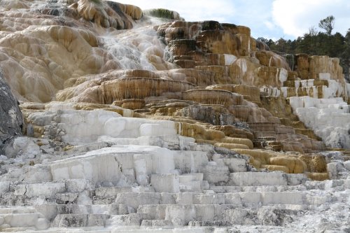 Terraced mineral formations with vibrant colors and cascading water, resembling a natural hot spring landscape.