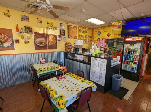Cozy restaurant interior with sunflower tablecloths, colorful decor, and a counter displaying menu items and drinks.
