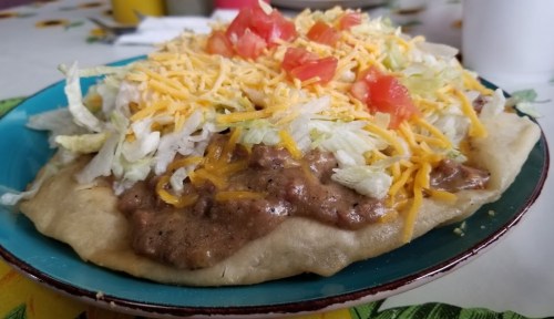 A colorful plate of a taco salad topped with lettuce, cheese, tomatoes, and refried beans on a crispy shell.