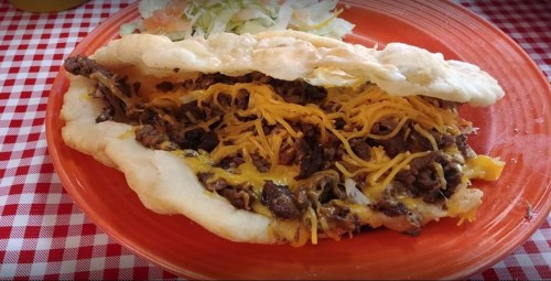 A plate featuring a stuffed flatbread with beef and melted cheese, accompanied by a side of shredded lettuce.