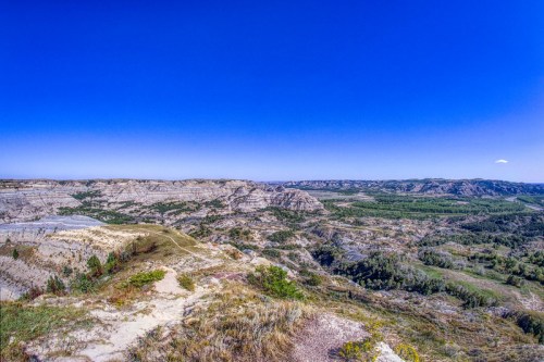 Panoramic view of rugged hills and valleys under a clear blue sky, showcasing the natural beauty of the landscape.
