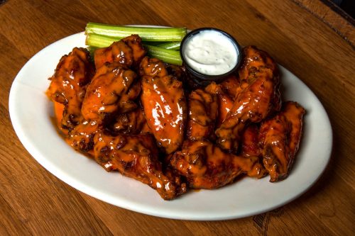 A plate of spicy chicken wings with celery sticks and a small bowl of ranch dressing on a wooden table.