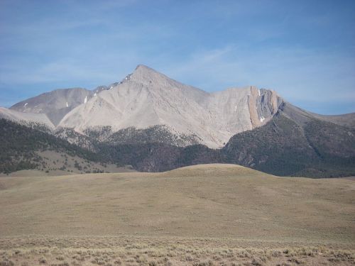 A rugged mountain peak rises above a grassy plain under a clear blue sky.
