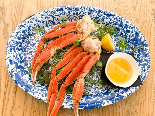 A platter of crab legs garnished with herbs, a lemon wedge, and a small bowl of melted butter on a blue speckled plate.