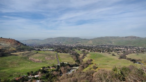 A panoramic view of rolling green hills and a valley with a small town under a clear blue sky.