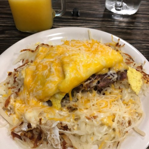 A plate of cheesy hash browns topped with eggs and meat, alongside a glass of orange juice.