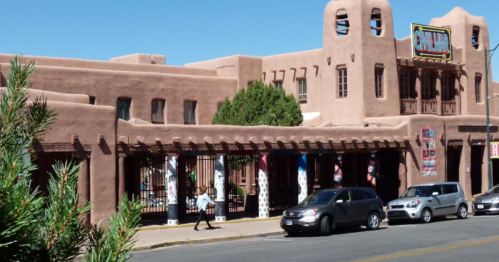 A southwestern-style building with adobe architecture, featuring a sign and parked cars in front.
