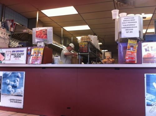 A fast-food counter with a cook preparing food, menus displayed, and a sign for a cheeseburger special.