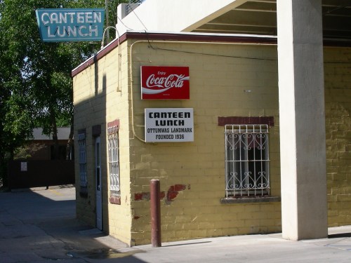 A yellow building with a sign reading "Canteen Lunch" and a Coca-Cola advertisement, featuring a vintage style.