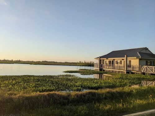 A serene lakeside house with a porch, surrounded by water and greenery under a clear blue sky.