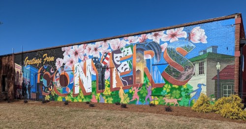 Colorful mural on a brick wall featuring the word "SOMYERS" surrounded by flowers and vibrant scenery.