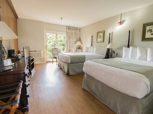 A spacious hotel room with two beds, a desk, and a view of greenery through sliding glass doors.