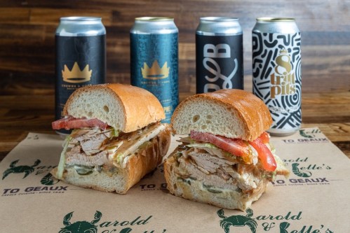 A close-up of a sandwich with turkey and toppings, flanked by four cans of craft beer on a wooden surface.