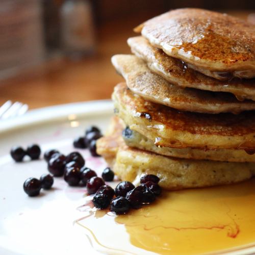 A stack of golden pancakes drizzled with syrup, accompanied by fresh blueberries on a white plate.