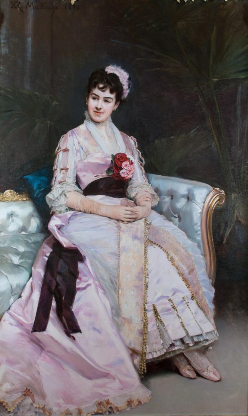 A woman in a pink gown sits elegantly on a sofa, holding a bouquet of roses, with a serene expression.