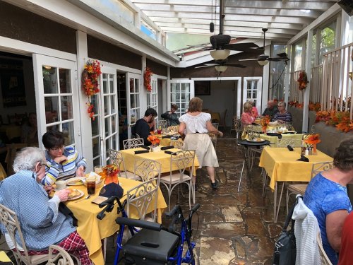A cozy restaurant patio with yellow tablecloths, diners enjoying meals, and autumn decorations.