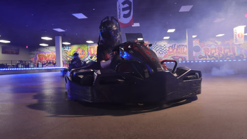 A go-kart racing on a track with colorful graffiti in the background and smoke effects, creating an exciting atmosphere.