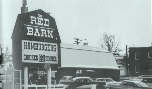 A vintage black-and-white photo of a restaurant sign reading "The Red Barn" with cars parked outside.