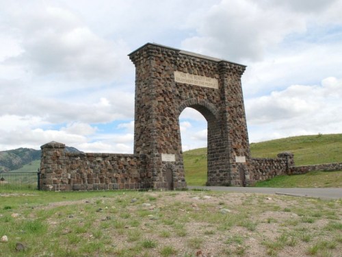 Stone archway monument with a plaque, set against a backdrop of green hills and cloudy skies.