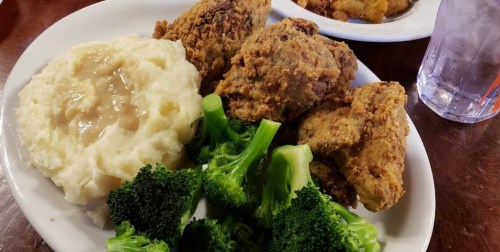 A plate of fried chicken, creamy mashed potatoes with gravy, and steamed broccoli, served with a glass of water.