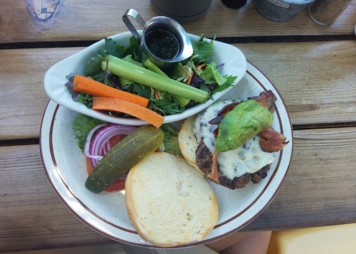 A plate with a burger topped with cheese and bacon, served with a side salad and fresh vegetables.