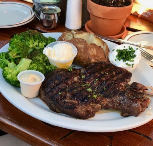 A plate featuring a grilled steak, baked potato with sour cream, and steamed broccoli on a wooden table.