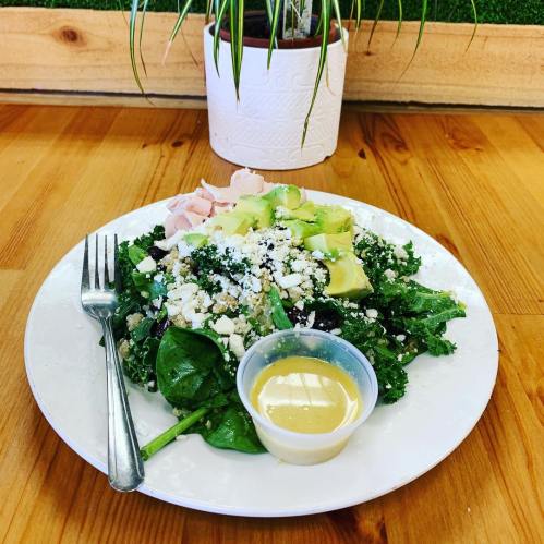 A fresh salad with kale, spinach, avocado, turkey slices, feta cheese, and a side of dressing on a white plate.